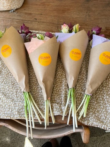 Four flower bouquets wrapped in brown kraft paper sleeves with yellow 'SUNNY' stickers, in Havelock North.